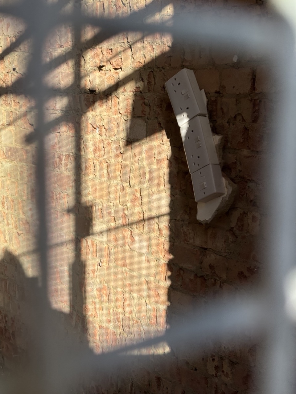 Photograph of electrical sockets and plasterboard hanging loosely from a crumbling brick wall